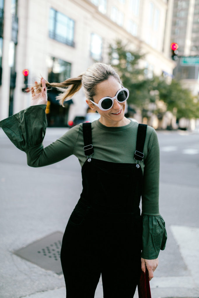 woman touching her hair and wearing velvet overalls