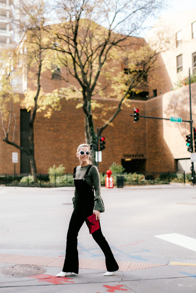 woman Pairing Velvet Overalls with a Statement Top and Velvet Clutch 